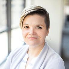 Katie Heiden Rootes, headshot. She is looking at the camera while wearing a grey sweater and light blouse.