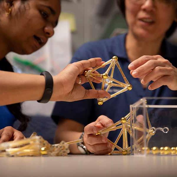 A group of students play with magnetic rods in a classroom as part of a demonstration of 3D shapes.