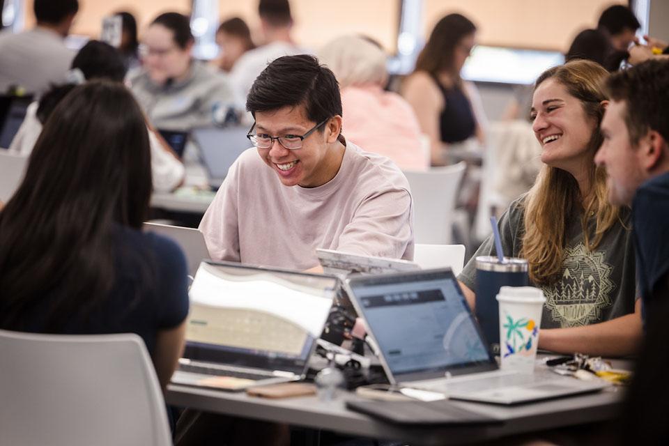 Students sit around a table with laptops studying.